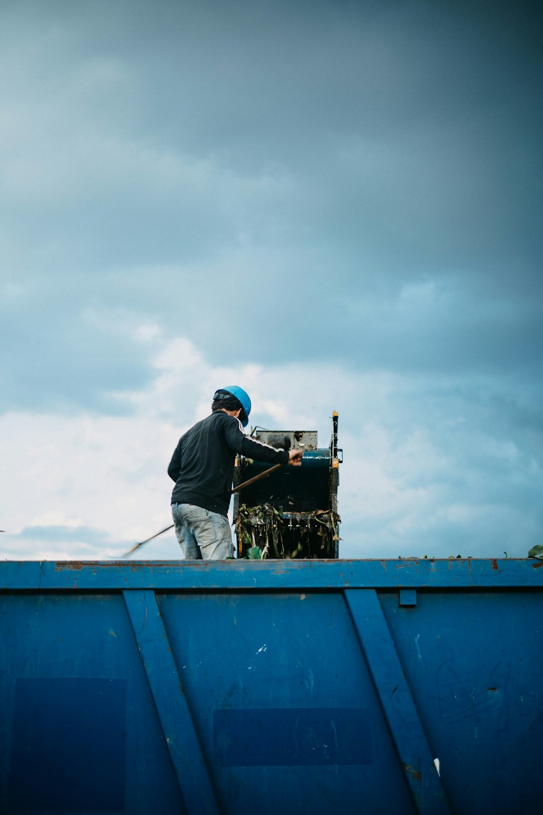 a-man-standing-on-top-of-a-blue-dumpster-r34b8raphfm