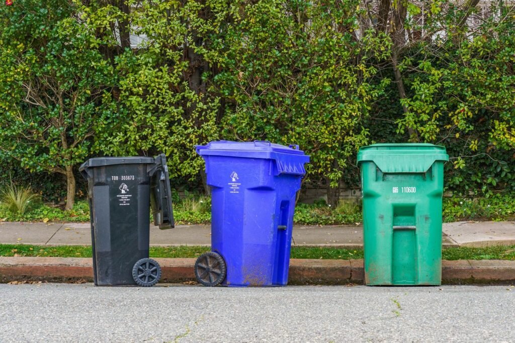 Black, blue, and green recycling bins on the street curb, ready for collection.